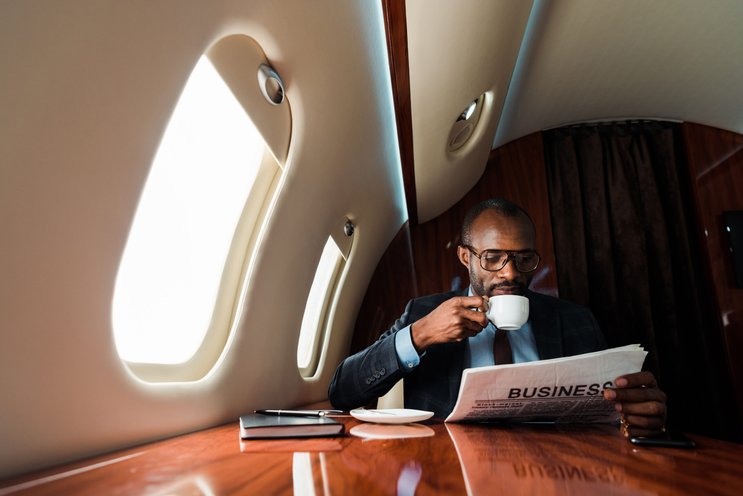 African American businessman reading business newspaper while drinking coffee in private plane